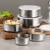 A set of stainless steel food containers with white lids, some filled with food items like pasta and beans, arranged on a wooden cutting board. Produktbild-Vorschau