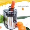 A stainless steel juicer with a carrot in the chute, surrounded by oranges and a cucumber. Náhled obrázku produktu