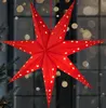 A red star-shaped lantern with small yellow lights is hanging in front of a window with blurred lights in the background. Podgląd zdjęcia produktu