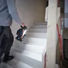 A person is walking up a concrete staircase holding a portable LED work light. Produktbild-Vorschau