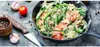 A close-up view of a cast iron pan filled with green beans and tomatoes, with garlic, a tomato, a knife, and peppercorns scattered around it. Produktbild-Vorschau