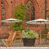 An outdoor seating area with wooden chairs and tables under umbrellas, next to a brick building with arched windows. Anteprima dell’immagine prodotto