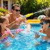 Drei Personen, ein Mann, ein Mädchen und ein Junge, spielen fröhlich mit drei verschiedenfarbigen Wasserpistolen in einem Schwimmbecken Produktbild-Vorschau