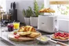 A breakfast spread featuring toast, croissants, jam, and juice on a kitchen counter. Produktbild-Vorschau
