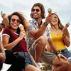 Three young adults are sitting together outdoors, each holding an ice cream cone and smiling. Náhled obrázku produktu
