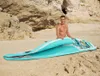 A man on a sandy beach is holding a partially folded inflatable paddleboard. Produktbild-Vorschau