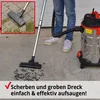 A person is using a wet/dry vacuum cleaner to clean up debris on a concrete surface. The vacuum cleaner is a large, metallic drum-style unit with a black and red top. A hose connects the vacuum to a wand with a floor brush attachment. The inset shows a clo Produktbild-Vorschau