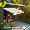 An awning is extended over a patio area next to a house, with greenery in the background. Náhled obrázku produktu