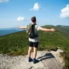 A person with a backpack stands on a rocky outcrop overlooking a forested mountain range. Náhled obrázku produktu