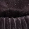 A close-up view of two different fabric textures, likely from a pet bed. The top fabric is dark and has small, raised black dots for grip. The bottom fabric is a plush, ribbed material in a dark gray color. Produktbild-Vorschau