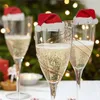 Champagne glasses decorated with Santa hats, set against a blurred Christmas tree background with lights. Produktbild-Vorschau