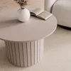 A round coffee table with a vase of dried flowers and an open book on it, placed on a textured rug next to a chair. Produktbild-Vorschau
