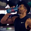 A man drinking from a shaker bottle in a gym. Produktbild-Vorschau