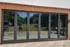 A person is reflected in a set of large, dark tinted bi-fold glass doors that open onto a garden. Anteprima dell’immagine prodotto