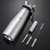 A stainless steel whipped cream dispenser with accessories is displayed on a reflective black surface. Produktbild-Vorschau