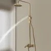 A gold-colored shower system with a rainfall showerhead and handheld showerhead is shown in use, with water spraying from the showerhead. Podgląd zdjęcia produktu