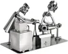 A metal sculpture of two figures working on a tattoo machine. Produktbild-Vorschau