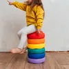 A young girl sits on a stack of rainbow-colored cushions, pointing to the left. Voir les images du produit