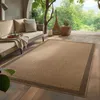 An outdoor living space with a sofa and a rug on a wooden deck, surrounded by greenery. Náhľad obrázku produktu