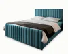A blue upholstered bed with white pillows and a dark throw blanket, presented on a white background. Produktbild-Vorschau