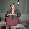 A woman holds a maroon tote bag in front of stacked chairs. Náhľad obrázku produktu