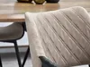 A close-up of a beige dining chair with diamond stitching, with a wooden table and another chair visible in the background. Podgląd zdjęcia produktu