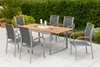 A patio dining set with a wooden table and chairs on a paved patio, surrounded by greenery. Náhled obrázku produktu
