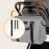 A gray diaper bag is attached to a stroller handle with straps. An inset shows three different strap options. Náhľad obrázku produktu