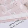 A close-up view of a pink sheer fabric with text printed on it, and a white elastic band. Produktbild-Vorschau