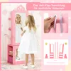 A young girl in a white dress is standing in front of a pink children's jewelry cabinet with a mirror. The image also includes close-ups of the anti-tip device and a diagram illustrating stability. Podgląd zdjęcia produktu