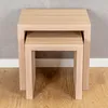 Two nesting tables made of light wood are shown against a textured gray wall and a white baseboard. Produktbild-Vorschau