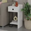 A white nightstand with a drawer and a shelf is placed next to a gray sofa. A large potted plant in a basket is to the right of the nightstand. Produktbild-Vorschau