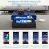 A modern coffee table with integrated LED lighting, shown in a living room setting with a sofa and a robot vacuum cleaner. Below the table are screenshots of a mobile app used to control the LED lights. Produktbild-Vorschau