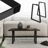 A coffee table with black trapezoidal legs, a dark wood top, a vase, and a mug on a rug in front of a sofa. Náhľad obrázku produktu