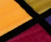 A close-up view of a textured blanket with a geometric pattern of colored squares separated by black lines. Produktbild-Vorschau
