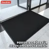 A black doormat is placed in front of an open glass door, on a tiled floor. Produktbild-Vorschau