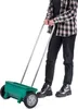 A person is pushing a green seed spreader on wheels. Podgląd zdjęcia produktu