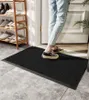 A person standing on a black doormat in front of a doorway, with a shoe rack visible to the left. Podgląd zdjęcia produktu