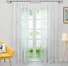 A bright room with a window covered by white sheer curtains with a leaf pattern. A yellow armchair with a pillow is in the foreground. Produktbild-Vorschau