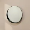 A round mirror with a black frame is mounted on a light pink wall, with a shadow cast on the wall. Produktbild-Vorschau