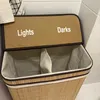 A laundry basket with two compartments, labeled 'Lights' and 'Darks', is shown in a bathroom setting. Produktbild-Vorschau