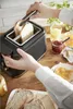 A person is making toast and preparing breakfast with jam, juice, and butter on a wooden countertop. Voir les images du produit