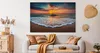 A living room scene with a large canvas print of a beach sunset above a sofa. Podgląd zdjęcia produktu