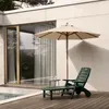 A dark green plastic sun lounger is placed on a wooden deck next to a pool, with a beige umbrella providing shade. Anteprima dell’immagine prodotto