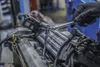 A person's gloved hand uses a wrench to tighten a spark plug on a car engine. Anteprima dell’immagine prodotto