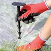 A person wearing red gloves and socks is using a black garden stake to secure white landscape fabric to the ground. Náhled obrázku produktu