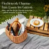 A picnic basket filled with bread, a bottle of wine, and books, placed on a blanket next to a wooden crate with a pastry on a plate. Produktbild-Vorschau