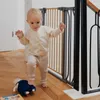 A baby is walking near a baby gate at the top of stairs, with a toy on the floor. Voir les images du produit
