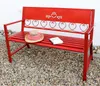 A red metal garden bench with a straw hat and a book on it, placed on a gravel ground. Produktbild-Vorschau