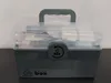 A gray and clear plastic medical kit storage box with a handle is shown on a dark surface against a light gray and white background. Náhled obrázku produktu